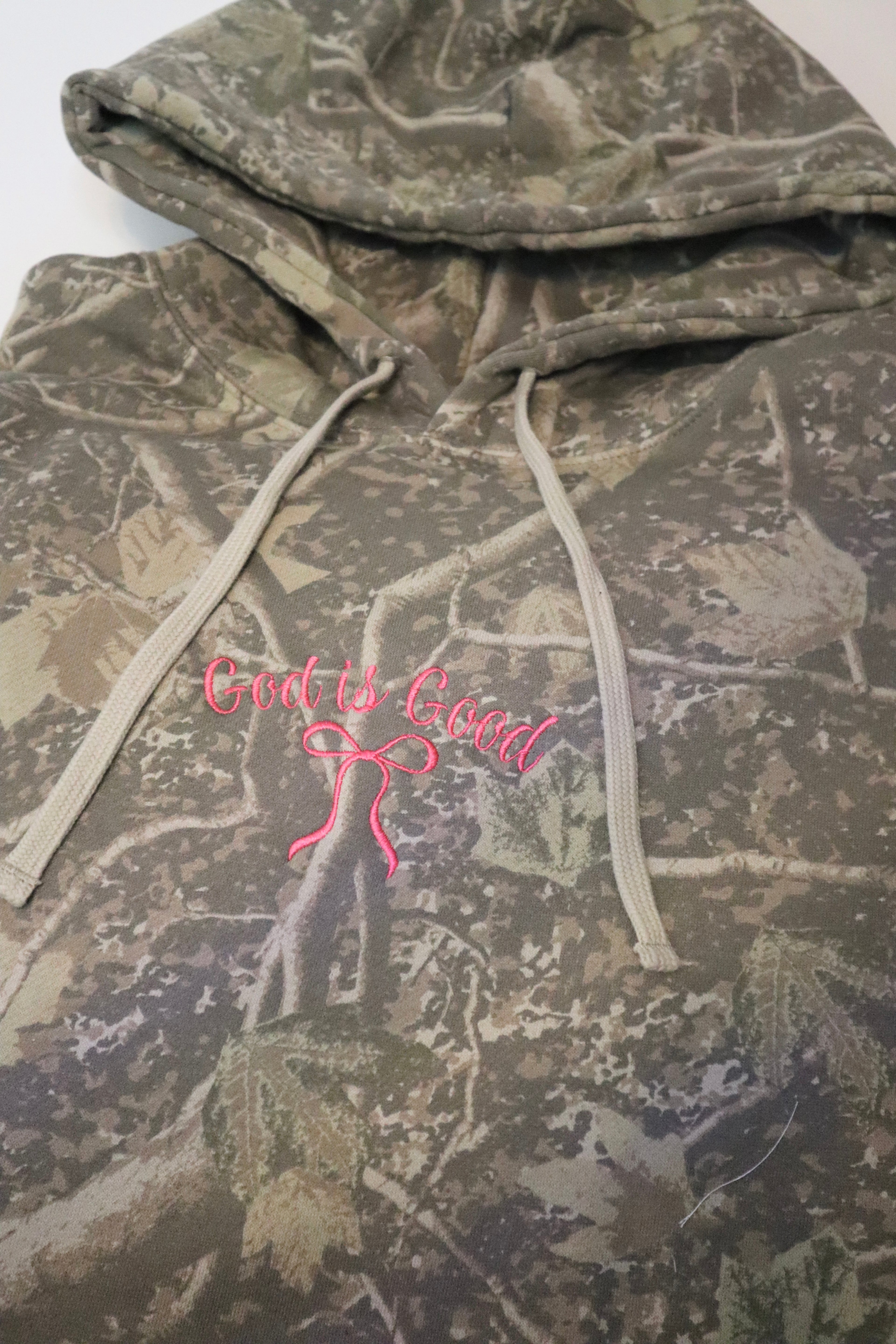 Camouflage hoodie with pink 'God is Good' text and design on a white background