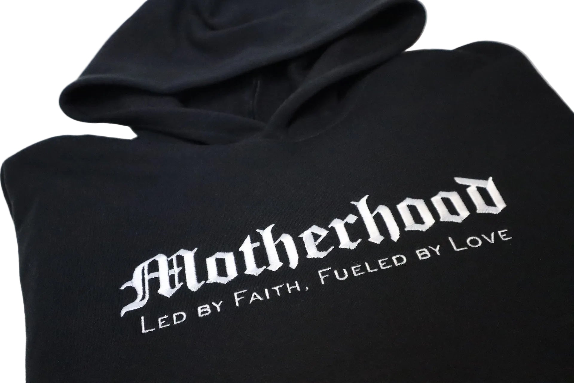 Black hoodie with 'Motherhood Led by Faith, Fueled by Love' text on a white background