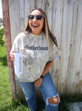 Load image into Gallery viewer, Woman wearing a &#39;Motherhood&#39; shirt and sunglasses, standing in front of a wooden fence.
